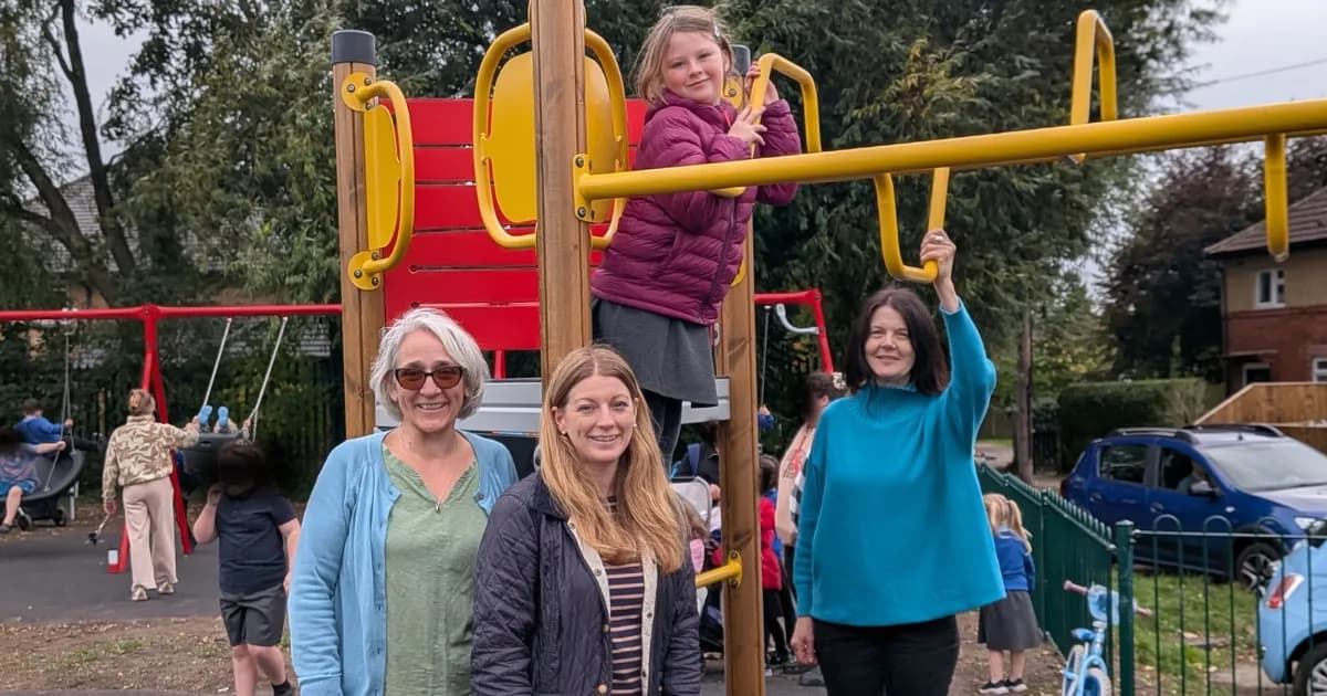 A young girl in a purple jacket on a yellow playground structure, with three women smiling in front of it.