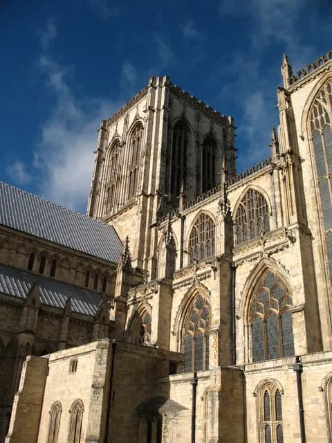 A grand Gothic cathedral with intricate stonework and stained-glass windows under a blue sky with white clouds.